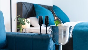 Una stanza con un divano blu, due bicchieri da vino, una bottiglia di champagne in un secchiello argentato e un comodino con una lampada.