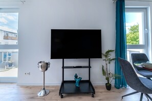 A modern living room with a flat-screen TV on a black stand, a silver trophy, a teal decorative item, a potted plant, and a grey chair.