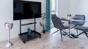 Un soggiorno moderno con una televisione a schermo piatto, un tavolino con sedie, una pianta e una coppa d'argento decorativa.