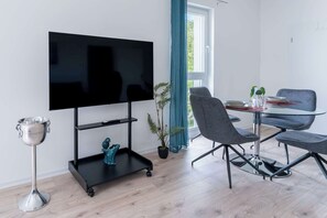 A modern living room with a flat-screen TV, a small table with chairs, a plant, and a decorative silver cup.