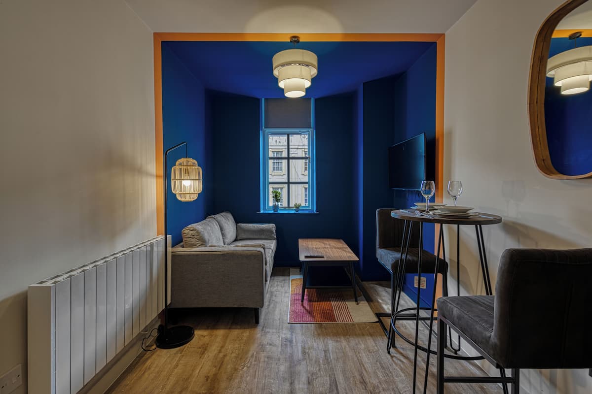 Un salon moderne avec un mur d’accent bleu, un canapé gris, une table basse en bois, une petite table avec un verre et un téléviseur fixé au mur.
