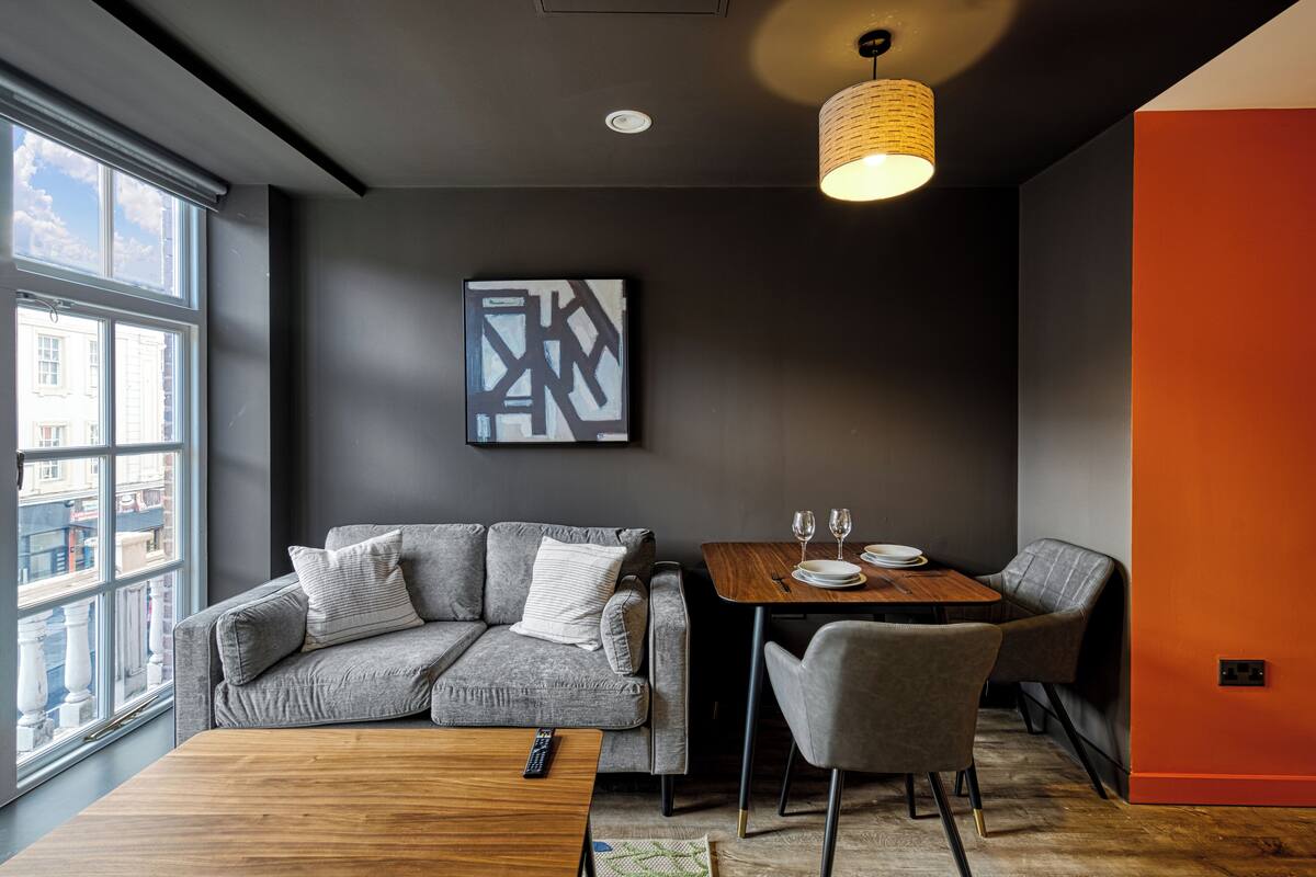 Un salon moderne avec un canapé gris, une table basse en bois et un coin repas comprenant une table et des chaises.