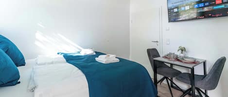Una habitación de hotel con cama, escritorio, silla, televisor en la pared y ventana.
