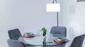 Un espace repas moderne avec une table en verre entourée de chaises grises, une plante en pot et un luminaire suspendu.