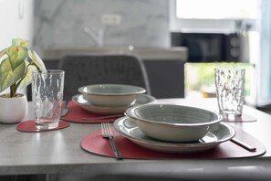 A dining table with plates, bowls, and a glass, set with red placemats and a fork.