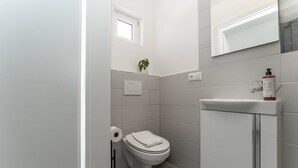 Un baño con inodoro, lavamanos, espejo y una pequeña ventana.