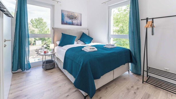 A bedroom with a bed, a bedside table, a window, and a view of the outdoors. - LiT LiVING: Luxus | Box SprIng | Kitchen | Parking (Altenstadt)