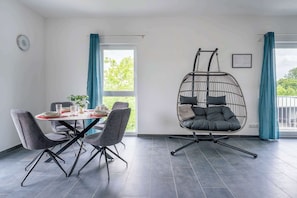 Ein Essbereich mit einem runden Tisch, grauen Stühlen und einem Hängesessel.