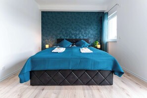 Ein modernes Schlafzimmer mit dunklem Kopfteil, türkisblau gestreuter Bettwäsche und einem Fenster mit Vorhängen.