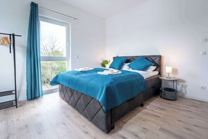 Una camera da letto con un letto, un comodino, una lampada, una finestra e una tenda.