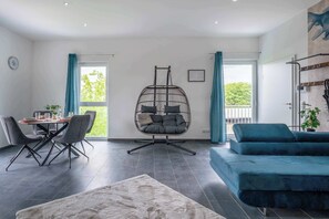 Ein modernes Wohnzimmer mit einem Esstisch, einem Hängekorbstuhl, einer Couch und einem großen Fenster.