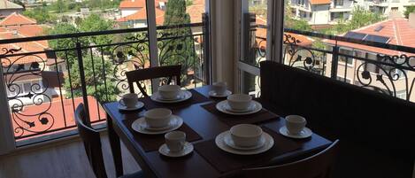 Un balcón con una mesa preparada para el té, con vistas a una zona residencial con edificios de tejados rojos.