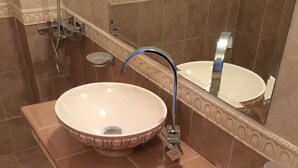 Un baño con un lavamanos color beige, un espejo y un cubo de basura.