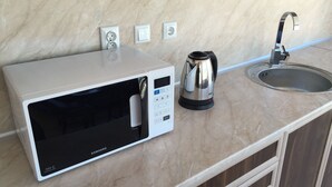 Una cocina con microondas, hervidor y pileta.