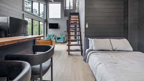 Ein modernes Blockhaus-Interieur mit einem Holztisch, einer Bar, einem Bett und einer Treppe.