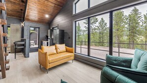 Ein modernes Interieur mit Holzbalkendecke, großen Fenstern, einer Couch und einem Essbereich.
