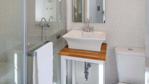 A modern bathroom with a glass shower enclosure, a white sink with a wooden countertop, and a toilet.