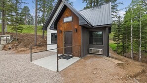 A small cabin with a wooden exterior and a metal roof, surrounded by trees. - Modern Black Hills Cabin · Romantic Getaway · Hot Tub · Near Deadwood (Sturgis)