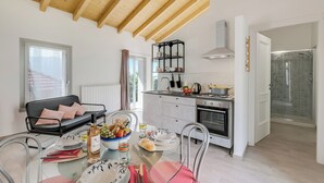 Une cuisine moderne avec un coin repas, des poutres en bois au plafond, une étagère en métal noir et une cabine de douche en verre.