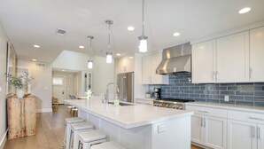 A modern kitchen with white cabinetry, a large island with bar stools, stainless steel appliances, and pendant lighting.
