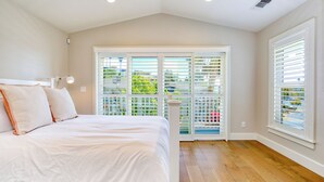 A bedroom with a large bed, a window with blinds, and a view of greenery outside.