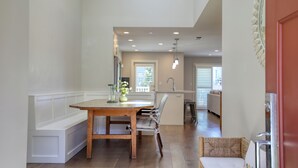 A spacious kitchen with a wooden table and bench, a white bench along the wall, and a view into the dining area.
