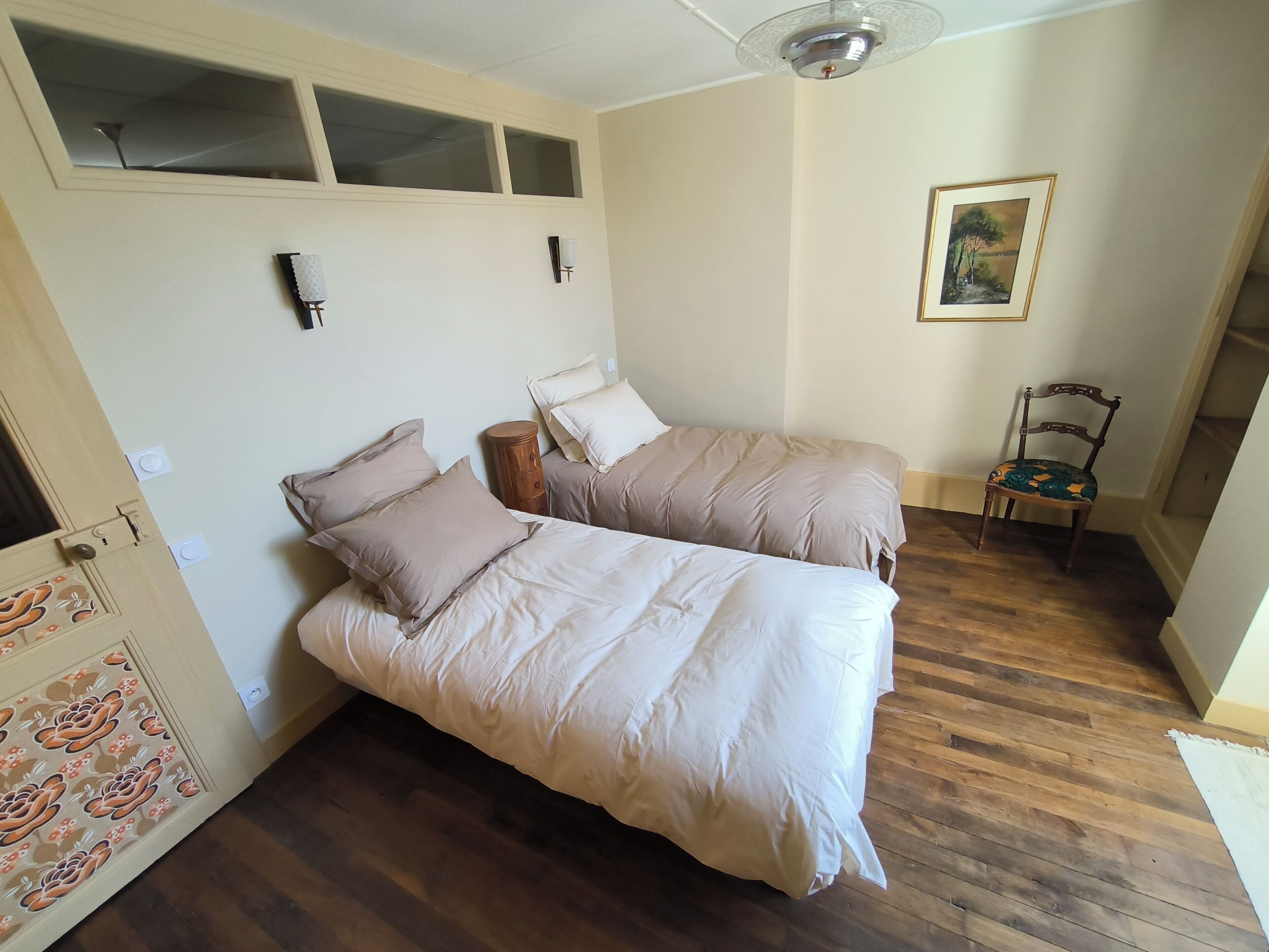 A bedroom with two beds, a wooden floor, a ceiling fan, and a painting on the wall.