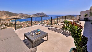 Uma varanda com vista para o mar e montanhas, mobiliada com uma mesa e cadeiras.
