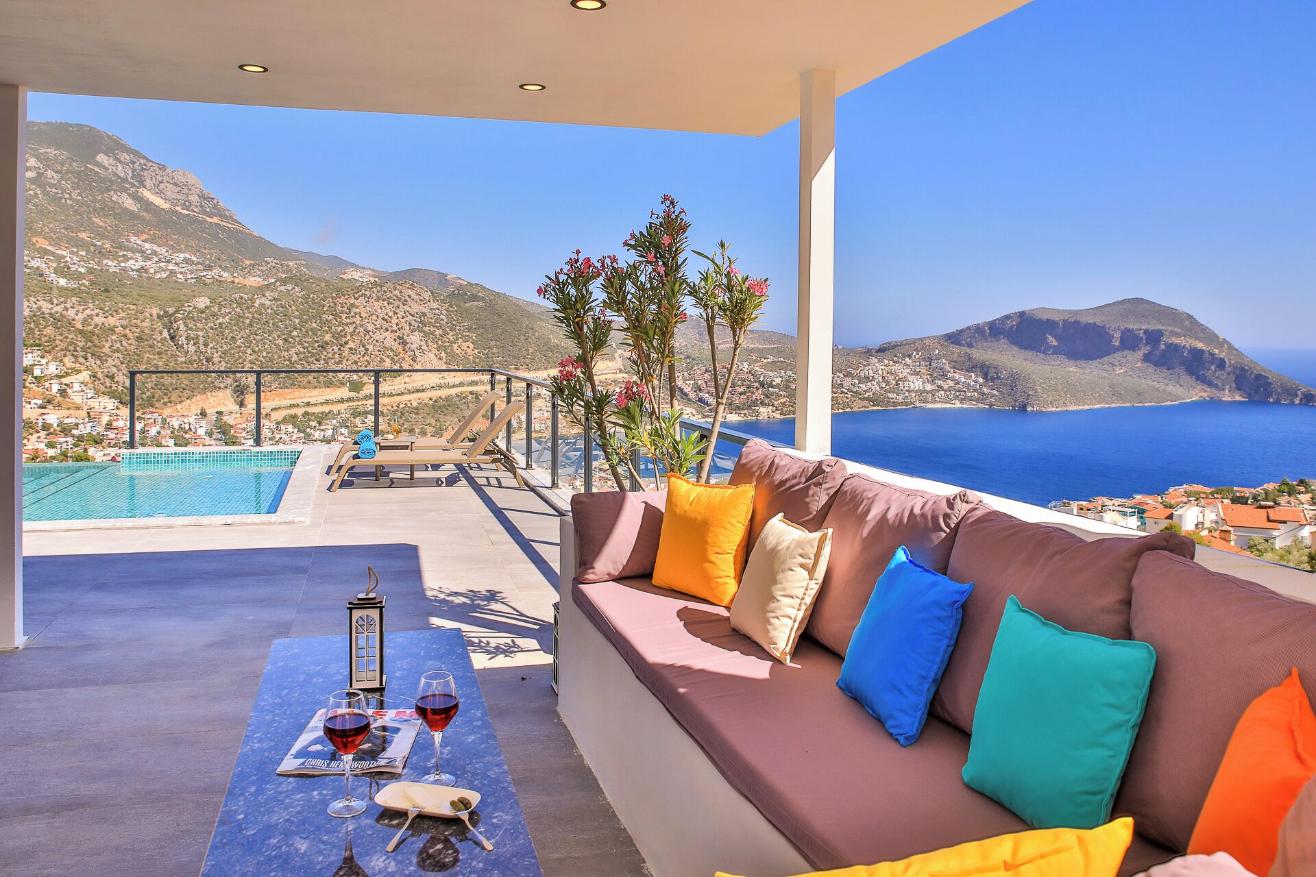 A modern outdoor seating area with a pool, a view of the sea, and a mountainous landscape.