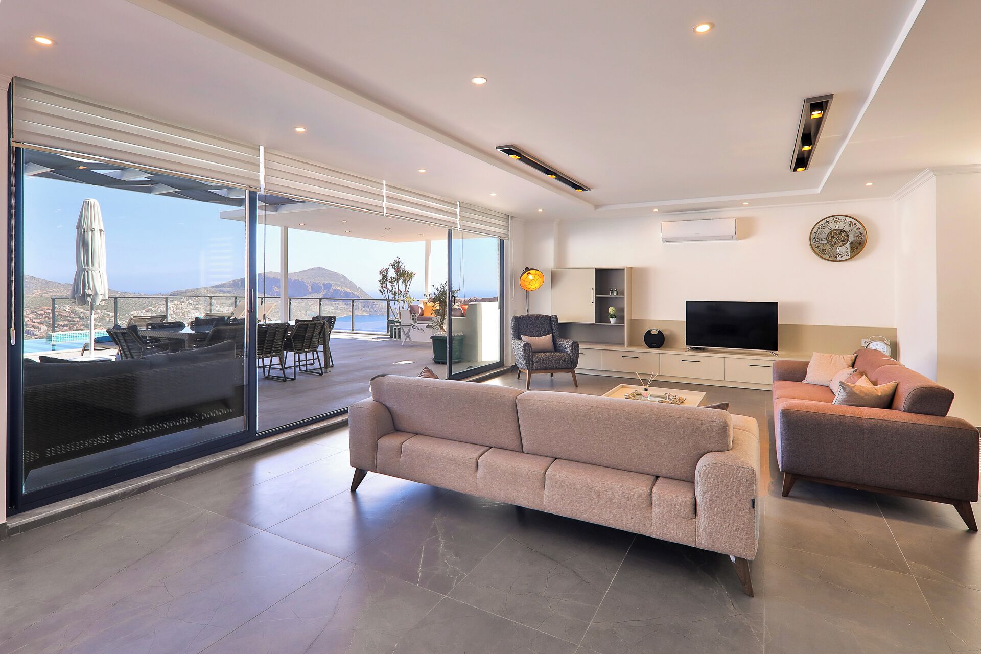 Amplia sala de estar con un gran ventanal corredera que da a una terraza exterior con piscina y sillas.