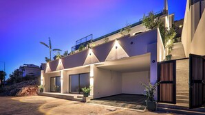 Um edifício moderno com telhado plano, grandes janelas e área de entrada pavimentada.