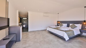 Quarto de hotel moderno com uma cama grande, mesas de cabeceira, televisão e banheiro visível através de uma porta aberta.