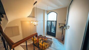 Una escalera conduce a una sala de estar con barandilla de madera, un candelabro y vistas al exterior a través de un ventanal.