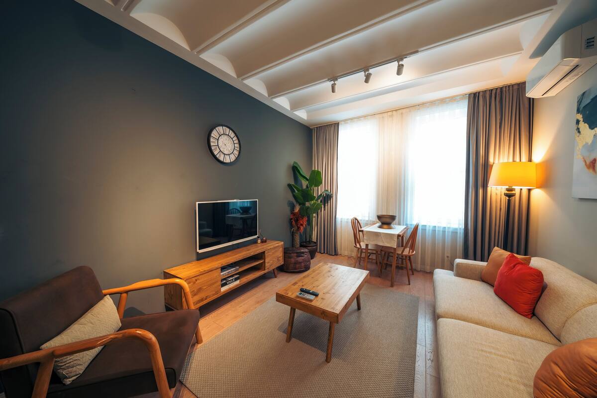 A modern living room with a sofa, armchair, coffee table, TV, and dining area.