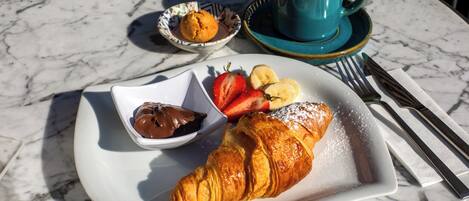 Ein Croissant, Erdbeeren, Bananen, Schokoladensauce und eine Tasse Kaffee auf einer Marmortischplatte.