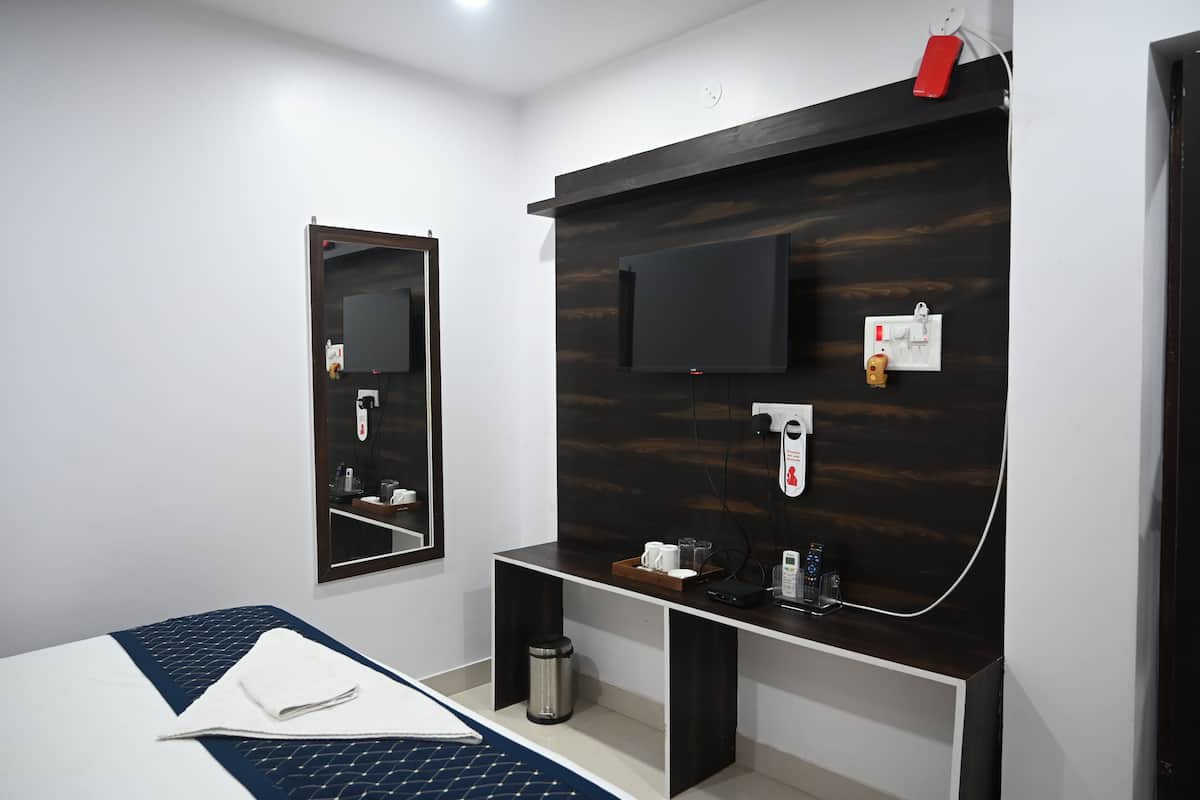 Ein modernes Hotelzimmer mit einem Bett, einem kleinen Schreibtisch, einem Spiegel, einem an der Wand montierten Fernseher und einer Kaffeemaschine.