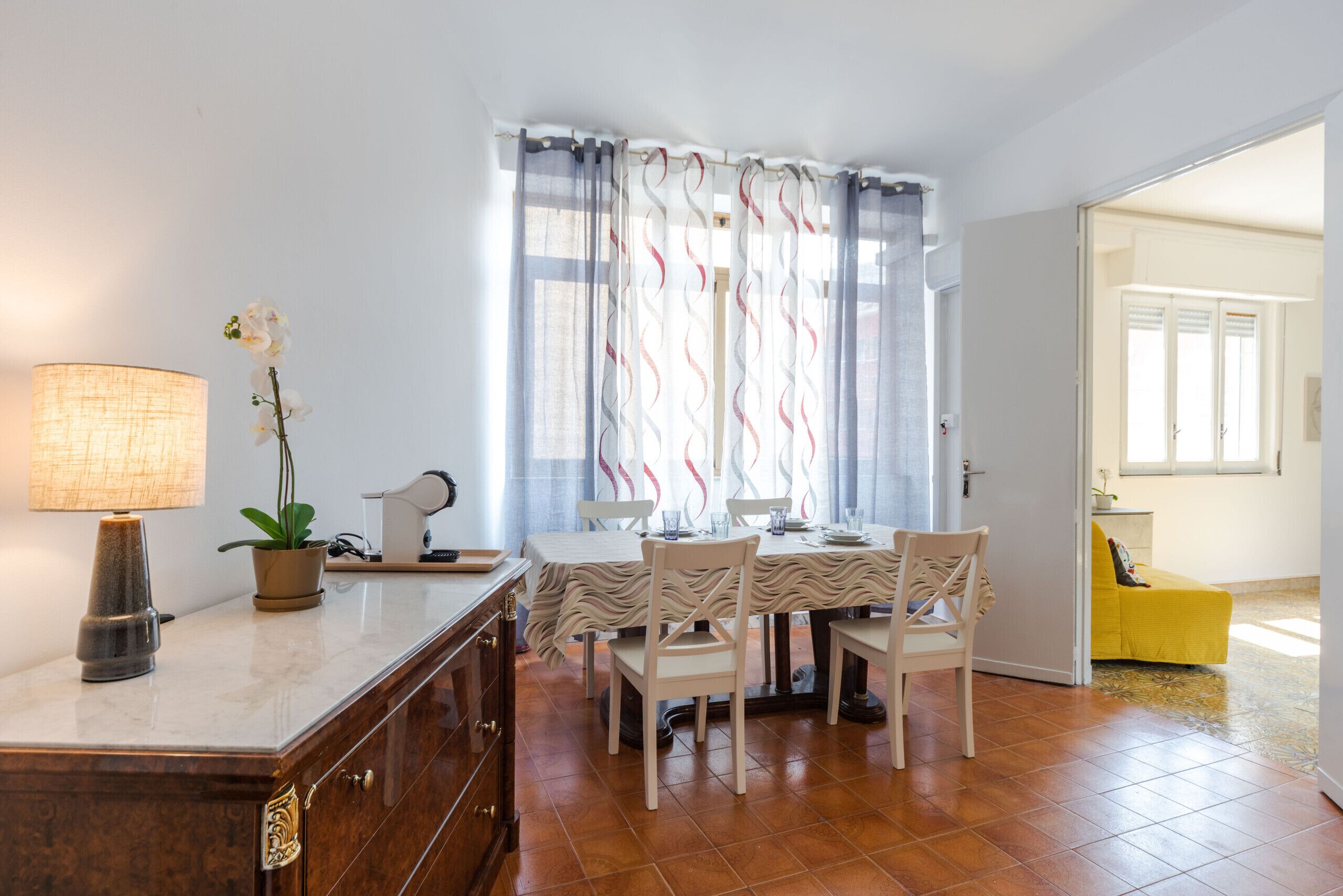 Un coin repas avec une table dressée pour quatre personnes, une lampe, une plante en pot et une chaise au design original.