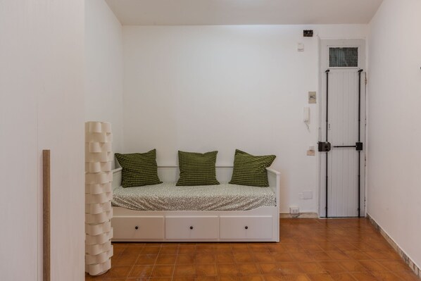 A small, single-bed room with a white wall, a wooden door, and a tiled floor.
