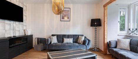 A modern living room with a large flat-screen TV, a grey sofa, a black entertainment unit, and a unique black and silver storage unit.