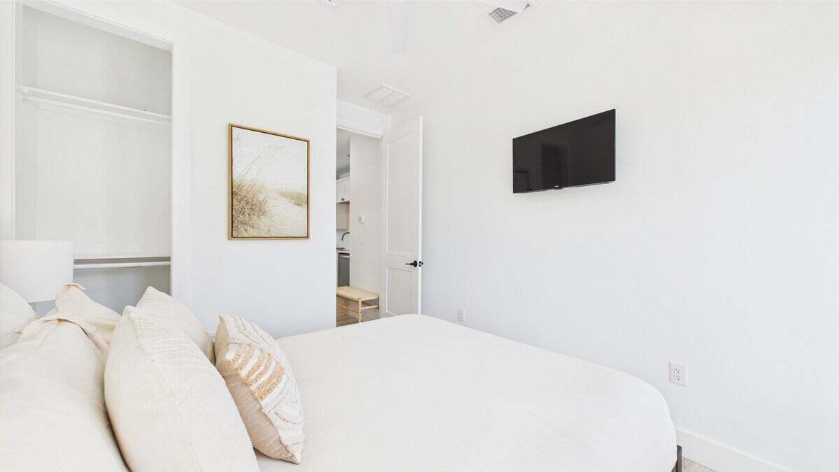 A bedroom with a bed, pillows, a TV mounted on the wall, and an open door leading to a bathroom.