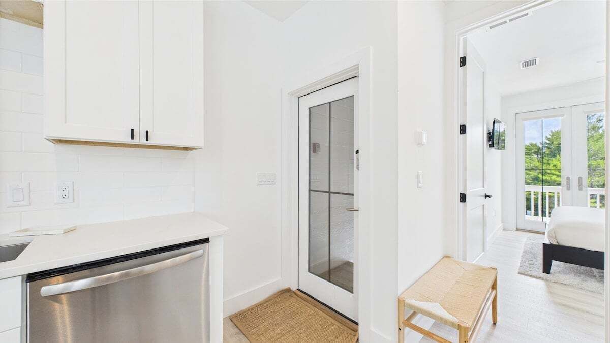 A modern kitchen with white cabinets, a dishwasher, and a sliding glass door leading to a balcony.