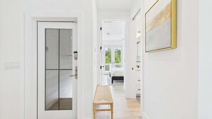 Un corridoio con una porta in vetro, una panca e un letto in lontananza.