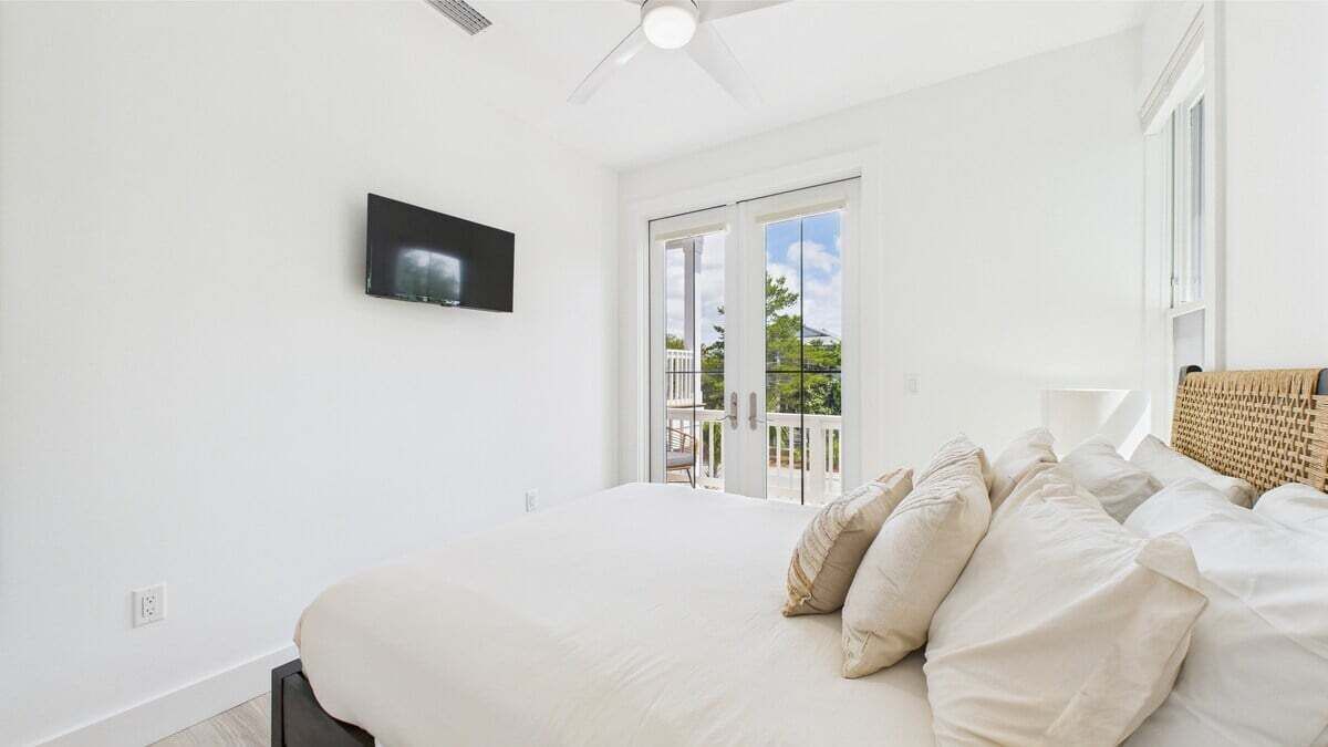 A bedroom with a bed, a television on the wall, and a balcony with a view.