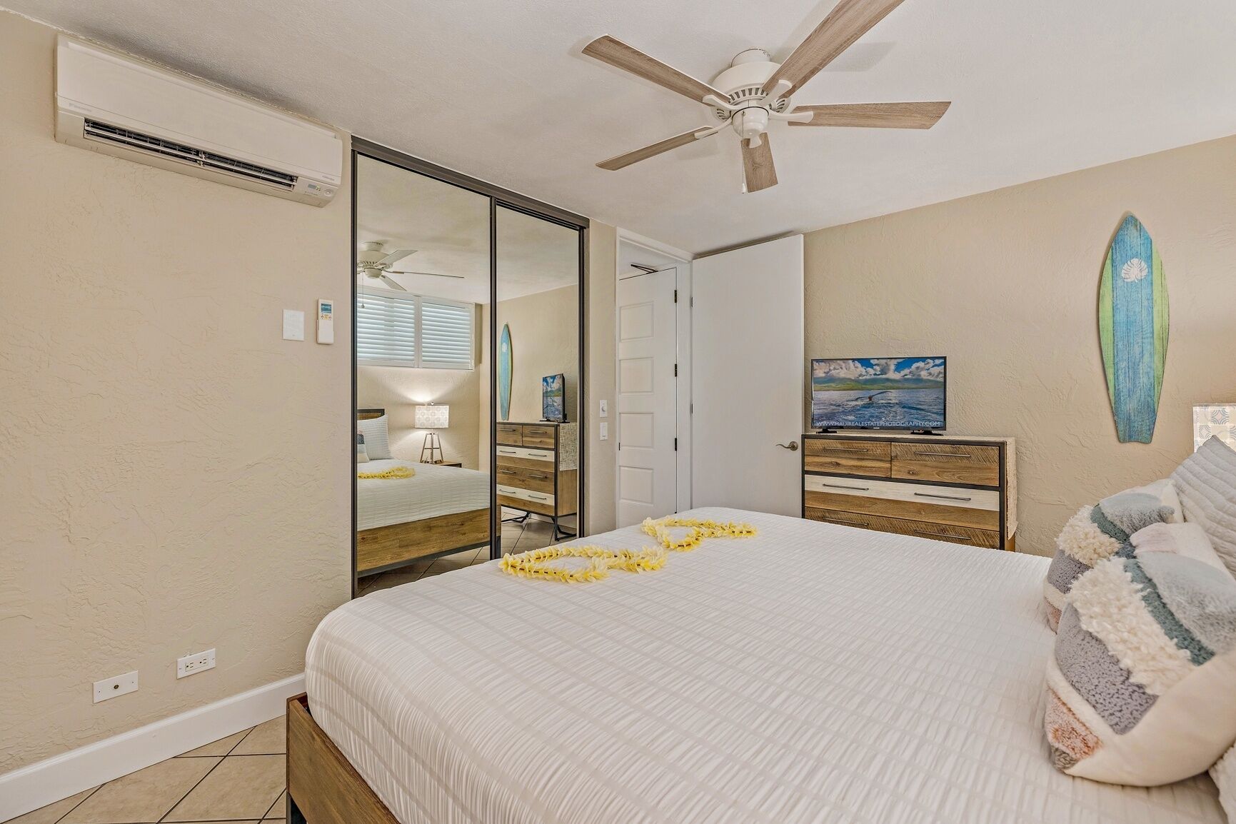 Un dormitorio con cama, ventilador de techo, cómoda, espejo y decoración con una tabla de surf.