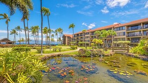 A hotel with a large pool surrounded by tropical plants and palm trees, with a view of the ocean. - Papakea G101 1bed/1bath New Remodel 1 Bedroom Condo (Lahaina)