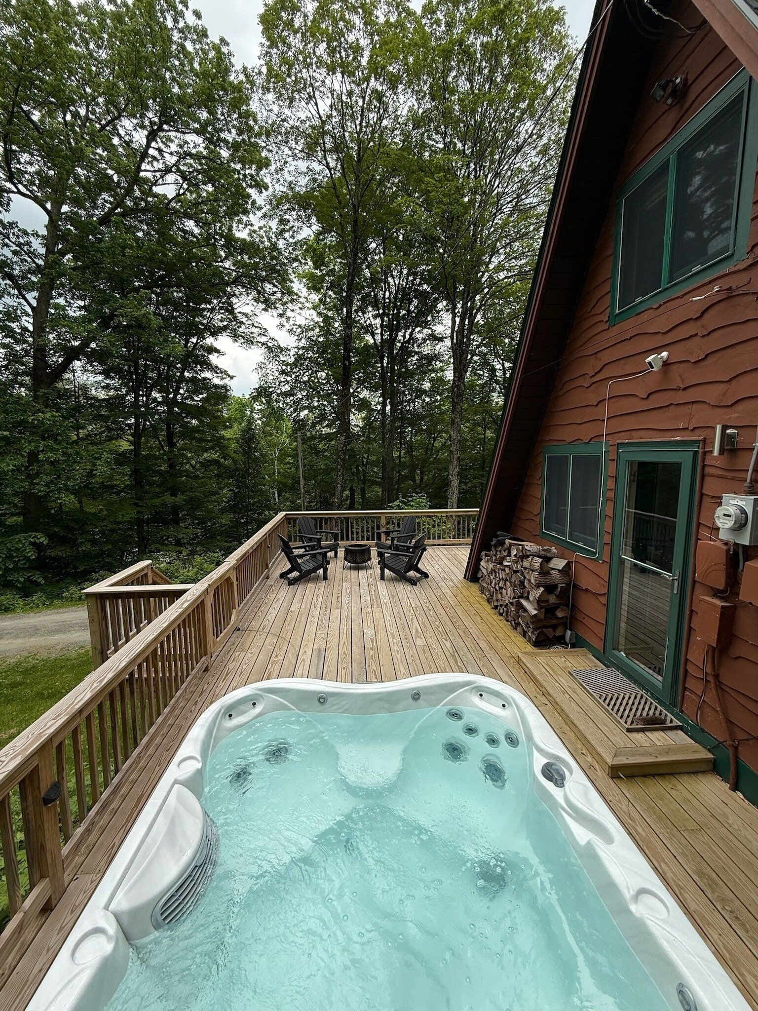 A hot tub on a wooden deck with outdoor seating and a view of a forested area.