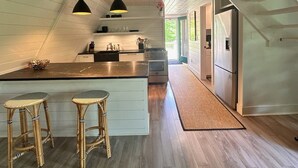 A modern kitchen with a central island, wooden flooring, and pendant lighting. - Killington A-frame 2 Bedroom Home (Killington)