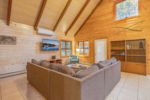 L’intérieur d’une cabane en rondins, avec un grand plafond en bois, un téléviseur fixé au mur, un canapé, une lampe et une bibliothèque.