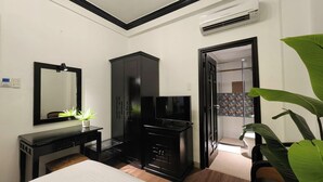 A hotel room with a bed, a desk with a computer, a TV, a wardrobe, and a large plant. - Rosa May Hotel (Ho Chi Minh City)