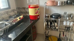 A kitchen with a gas stove, a red and yellow container, a pink pot, and a rack with various kitchen utensils. - 1BHK Comfy Stay 5 (Pune)